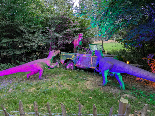 Three life sized model velociraptors attacking a jeep and a dinosaur park with Purple lighting on them.