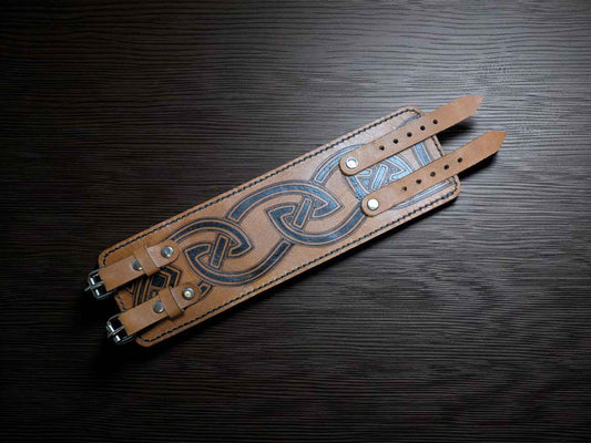 A Handmade Leather 'Norse Pattern' Viking Cuff Bracelet laid out on a dark brown tabletop.