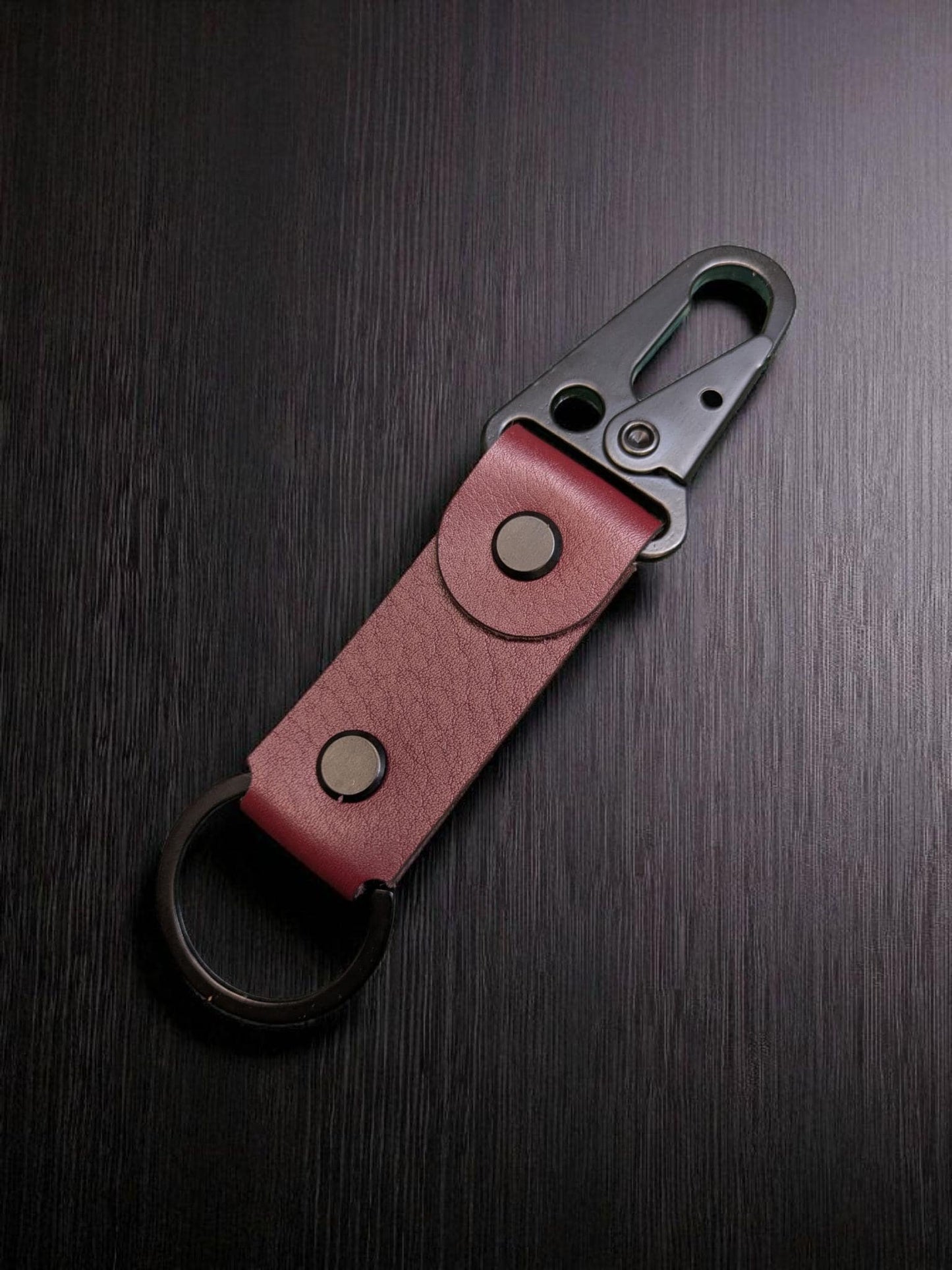 Backsdie of a Red leather keychain with metal clip on a dark wooden surface