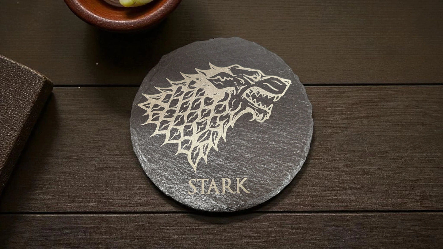 Slate coaster with Stark logo on a wooden surface