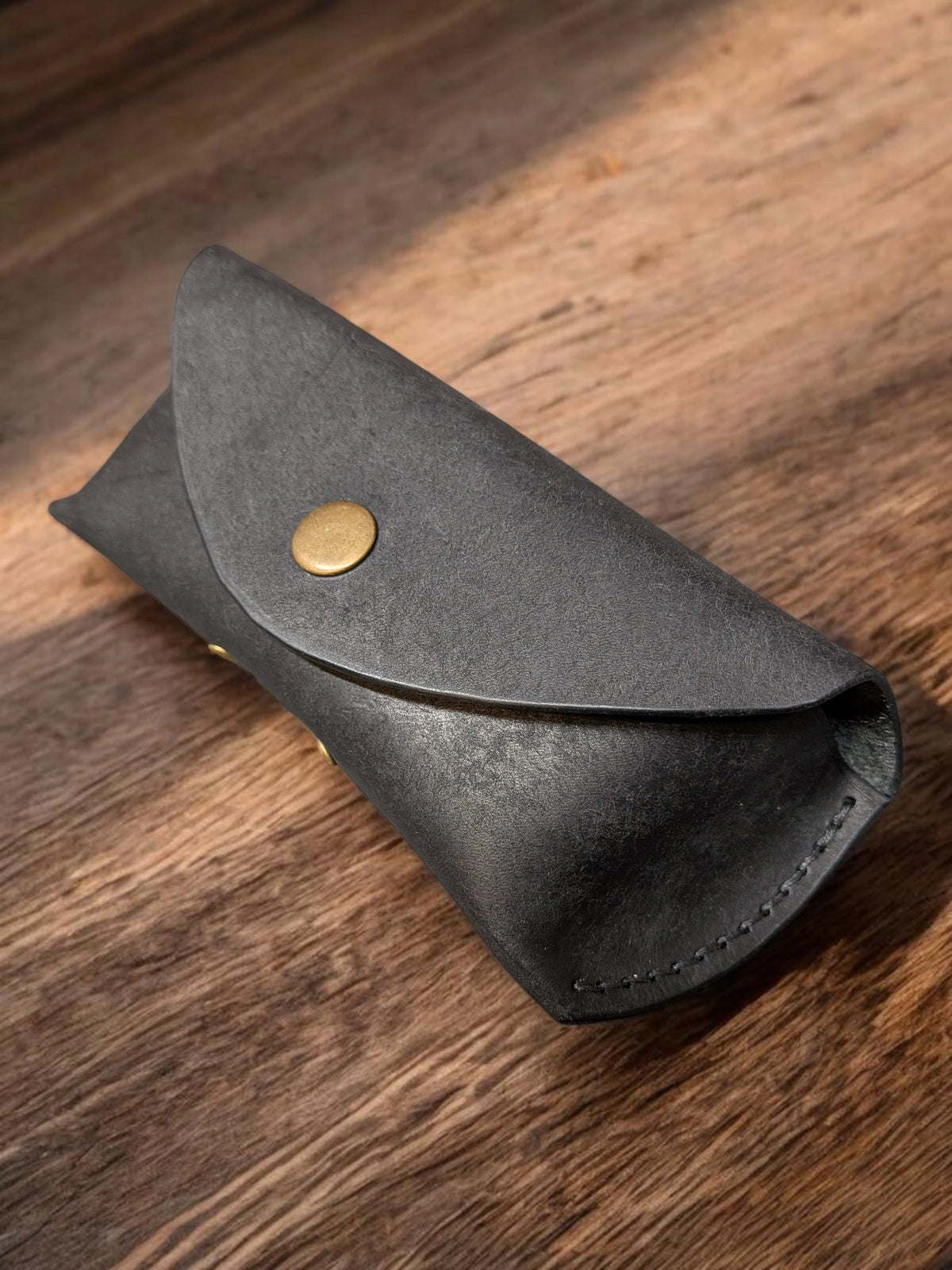 Handmade black leather sunglasses case in Badalassi Pueblo with brass snap closure, angled view