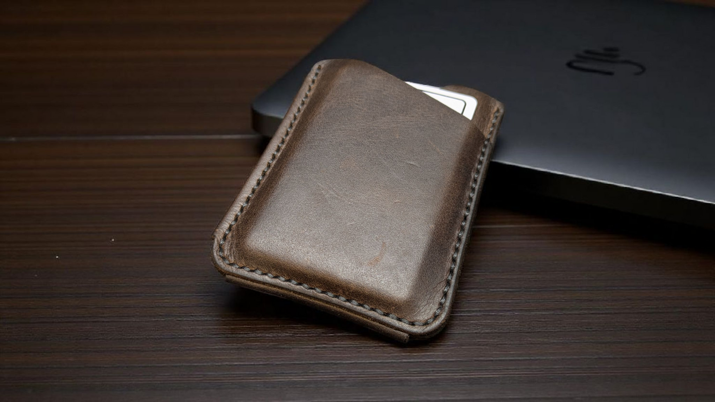 Brown full grain leather card holder wallet on a wooden surface with a black laptop in the background