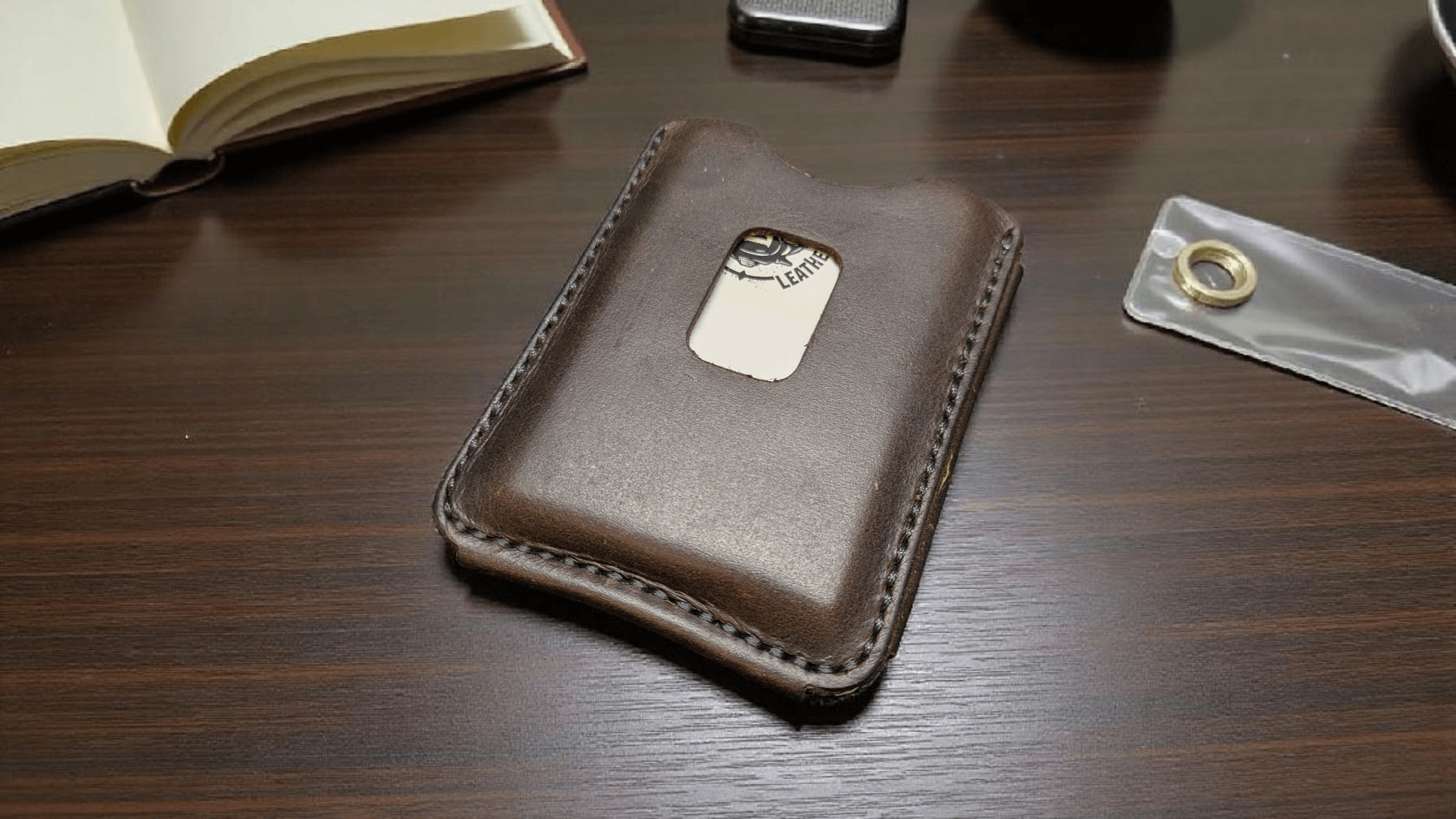 Brown full grain nubuck leather card holder wallet on a wooden surface with a book and small object in the background