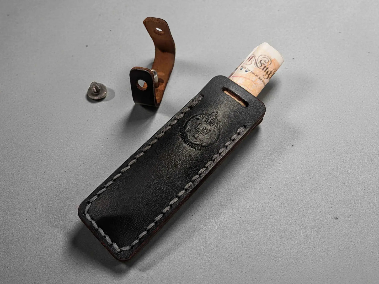 Black leather Cash Stash Keychain - Compact Emergency Cash Holder for Everyday Carry with stitched edges and embossed logo, showing rolled cash partially inserted and metal button detached.