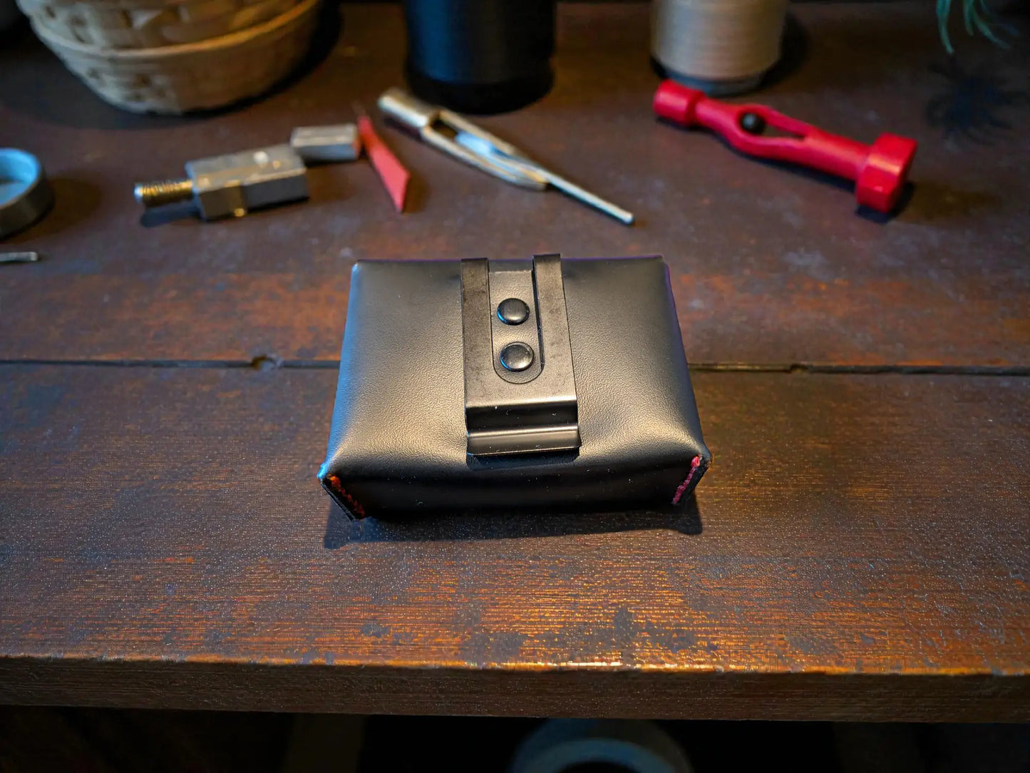 Custom Fire Service Alerter Case (Birdy & Multitone Type) made of smooth black leather with metal clip, placed on a wooden workbench with leatherworking tools in the background.