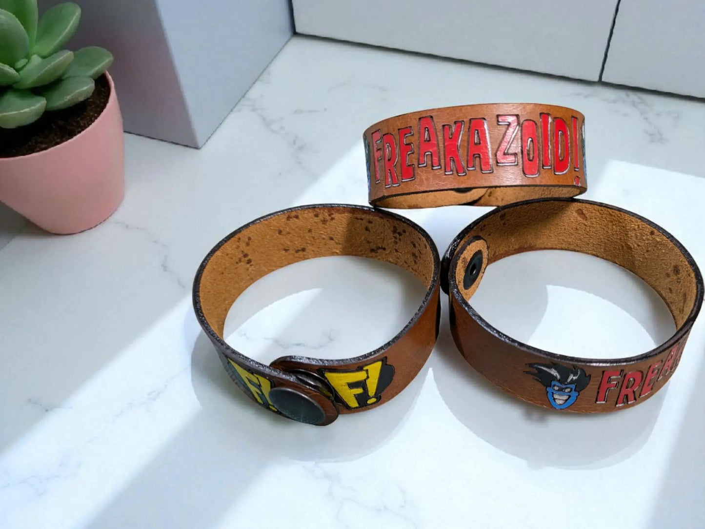 Brown leather wristbands with colorful freakazoid inspired leather branding and cartoon character designs on cuff bracelet
