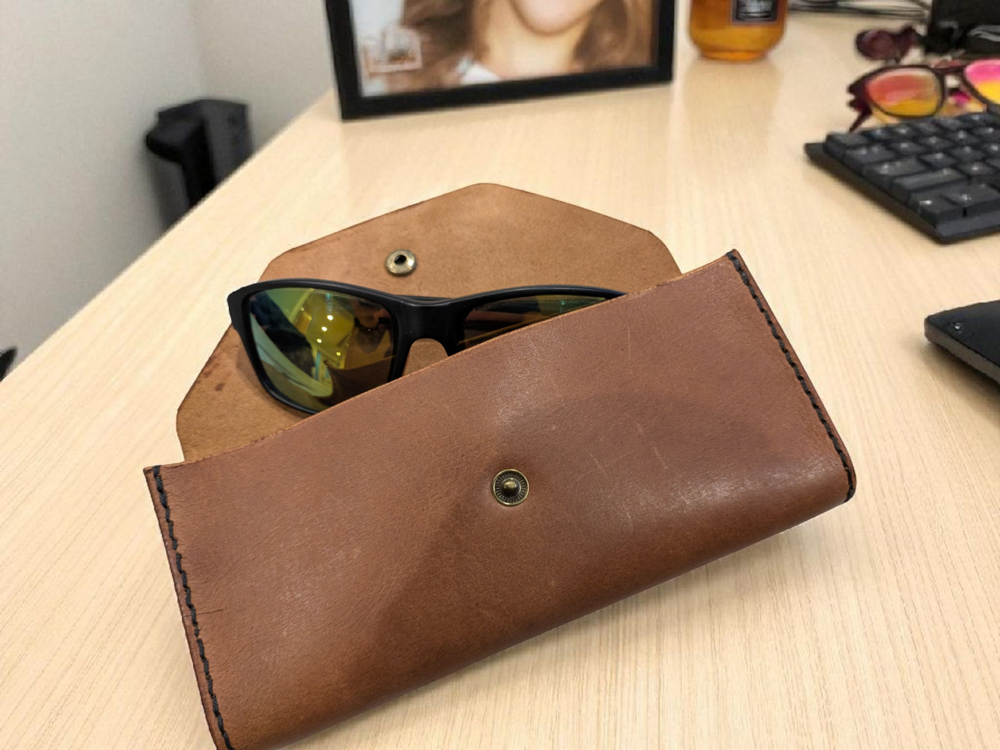 Brown leather sunglasses case with sunglasses inside on a wooden surface.