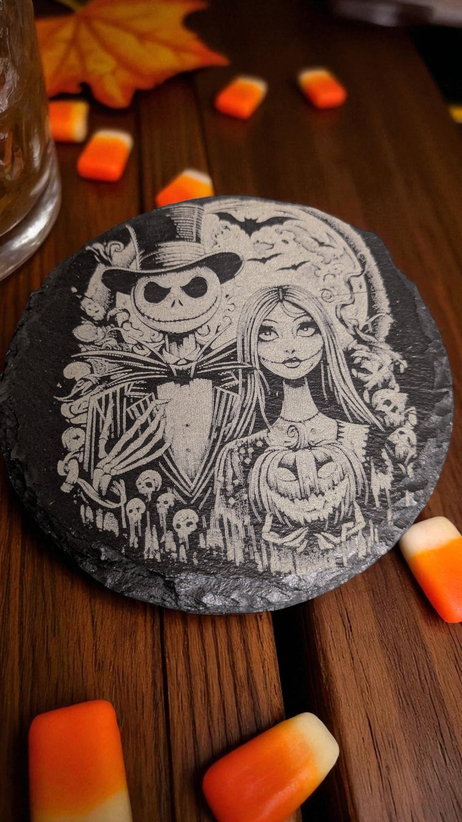 A Nightmare before Christmas Themed Engraved Drinks Coaster sat on a rustic workbench with halloween sweets next to it.