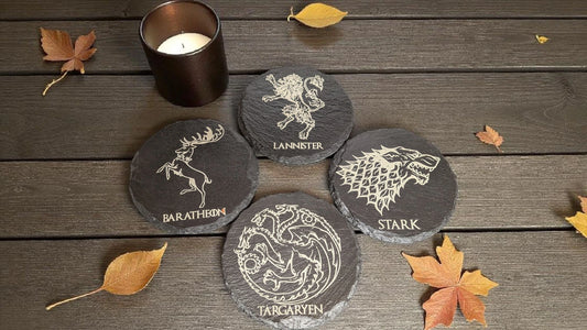 Set of Game of Thrones-themed coasters on a wooden surface with leaves and a candle.