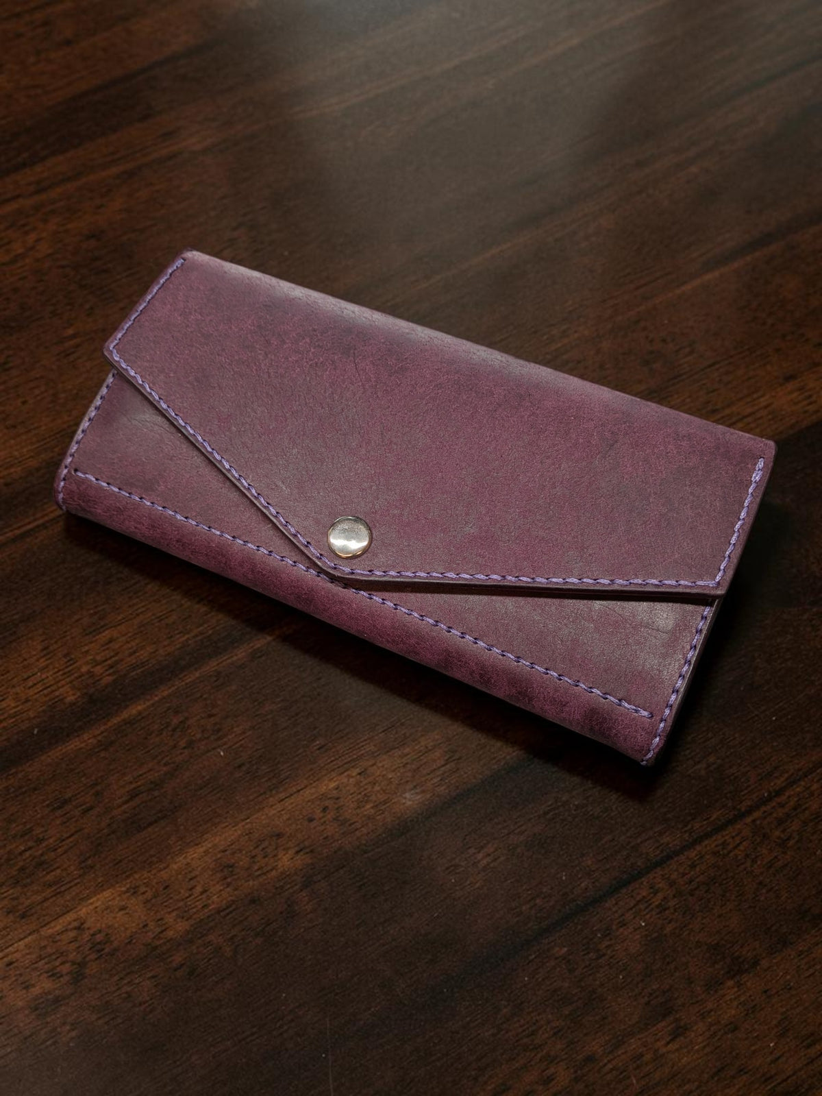 Ladies long wallet in purple Badalassi Pueblo leather with envelope flap, snap closure and lilac stitching, on a wooden table