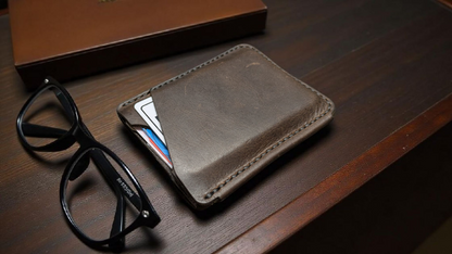 Brown full grain leather card holder wallet with glasses and cards on a wooden surface