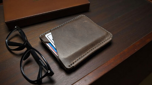 Brown full grain leather card holder wallet with glasses and cards on a wooden surface