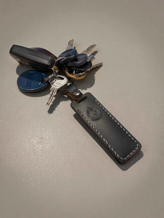 A set of keys attached to a black leather keychain with white stitching and embossed logo, featuring the Cash Stash Keychain - Compact Emergency Cash Holder for Everyday Carry.