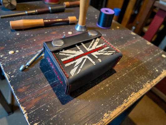 Custom Fire Service Alerter Case (Birdy & Multitone Type) made from black leather with a stitched Union Jack design and red trim, displayed on a wooden workbench with leather crafting tools.