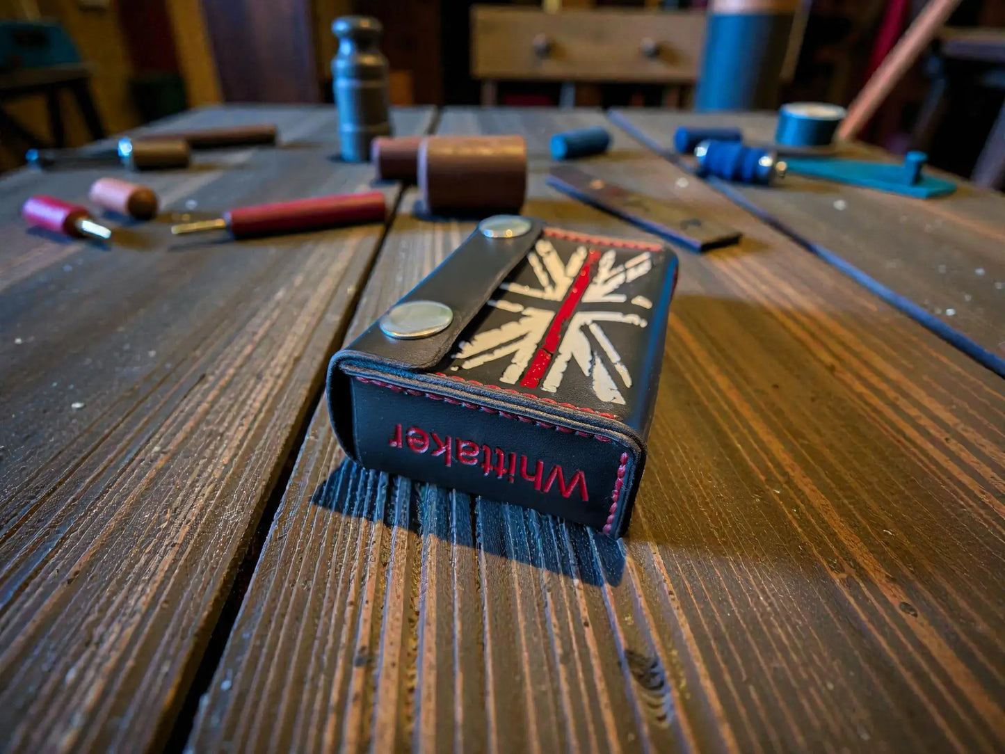 Custom Fire Service Alerter Case (Birdy & Multitone Type) on a wooden surface with leather crafting tools in the background, showcasing detailed stitching and design.