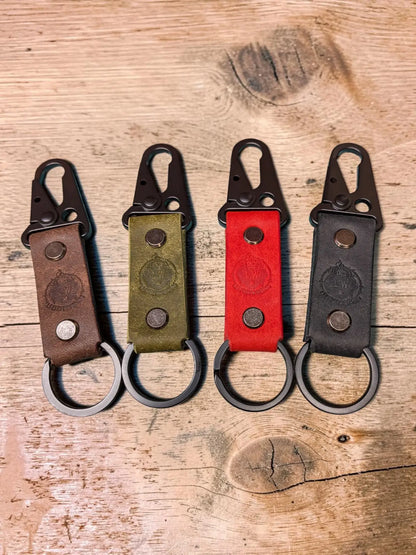 Four custom tactical leather keychains in brown, olive green, red, and black with metal carabiner clips and rings