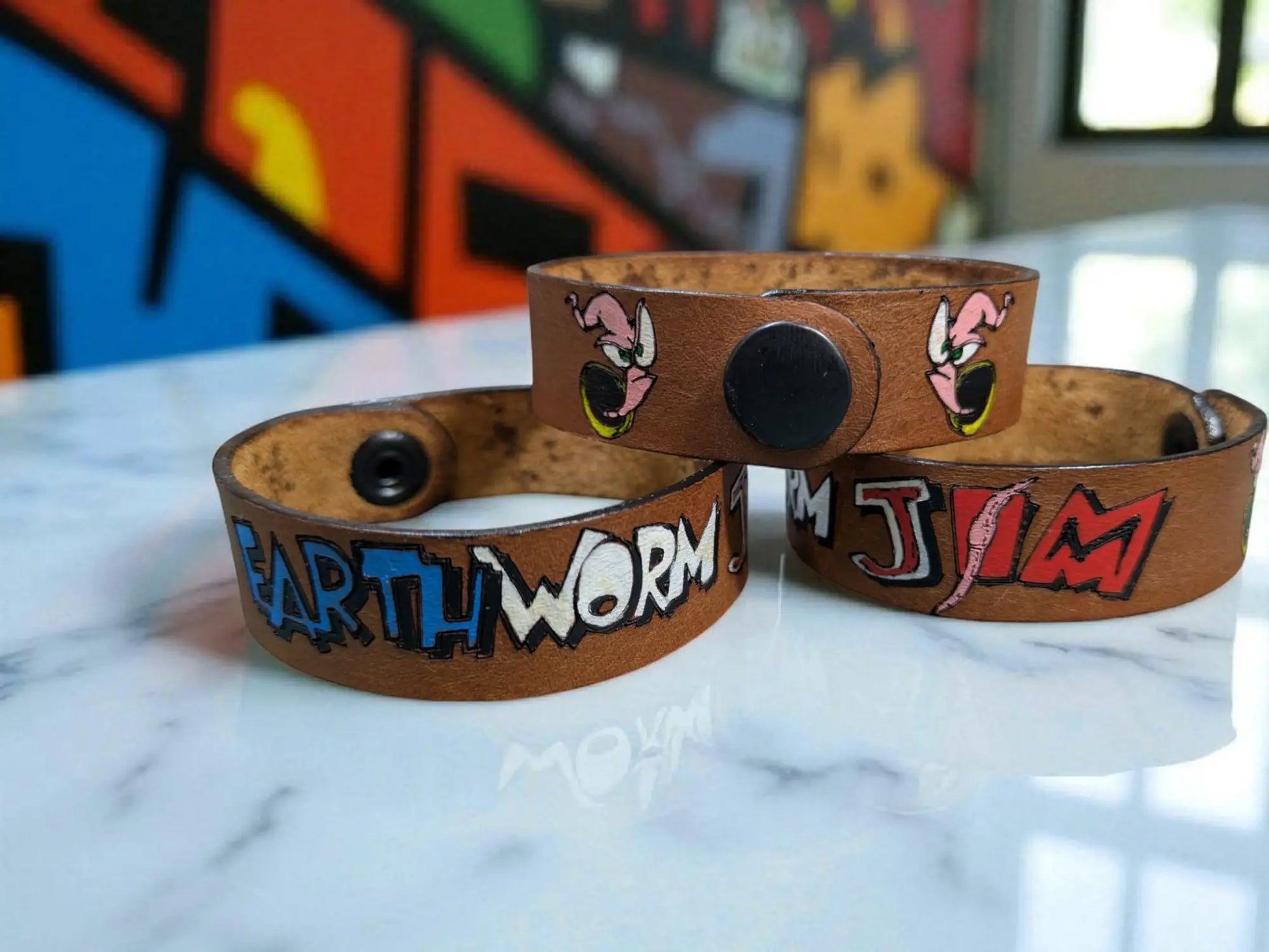 Brown leather wristbands featuring hand-painted earthworm jim designs and bold lettering in an earthworm jim inspired cuff bracelet