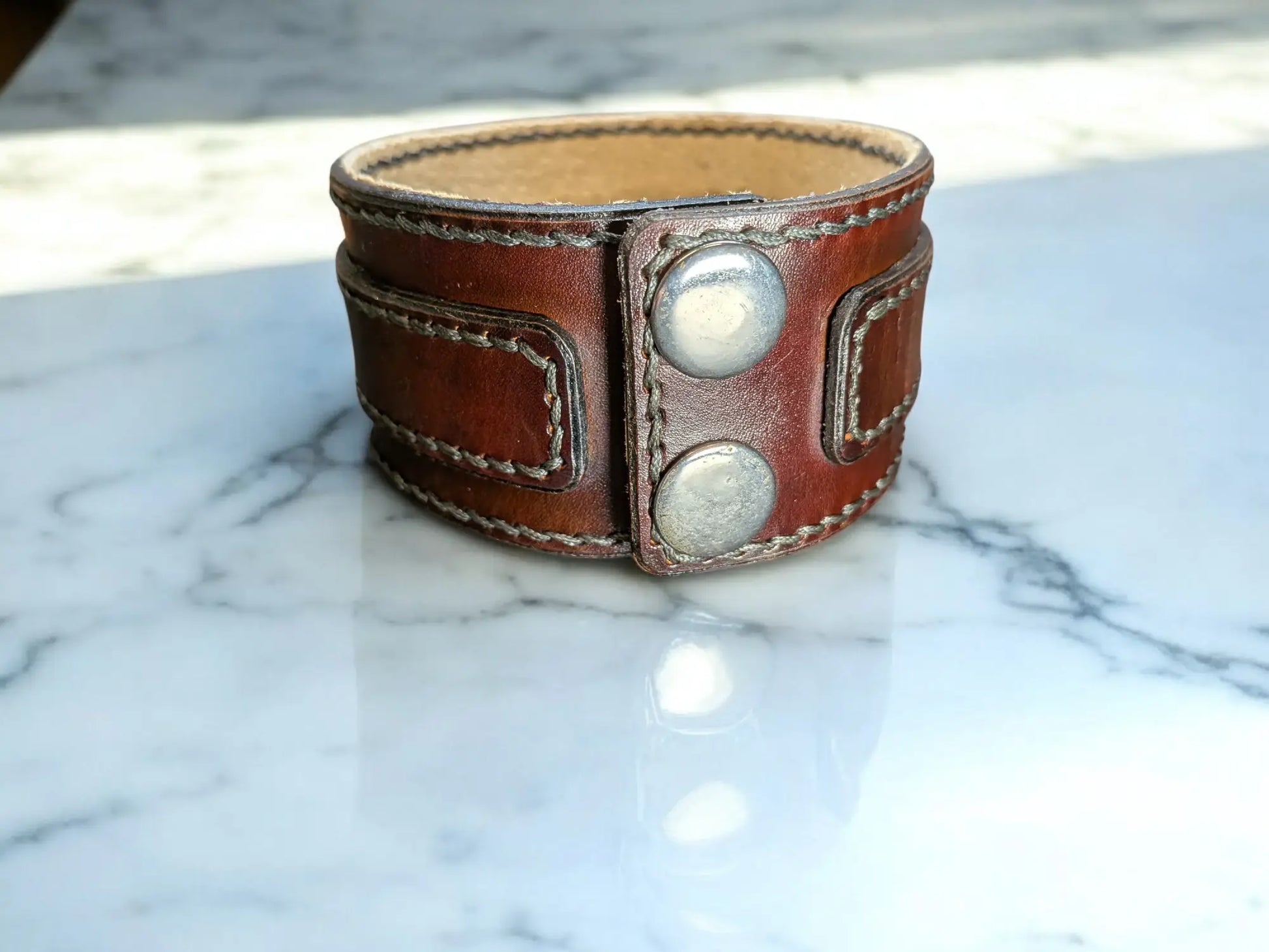 Brown full grain leather cuff bracelet with silver snap poppers on a marble surface
