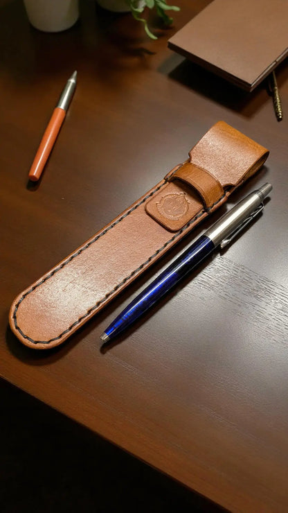 Brown leather pen holder with a pen on a wooden surface