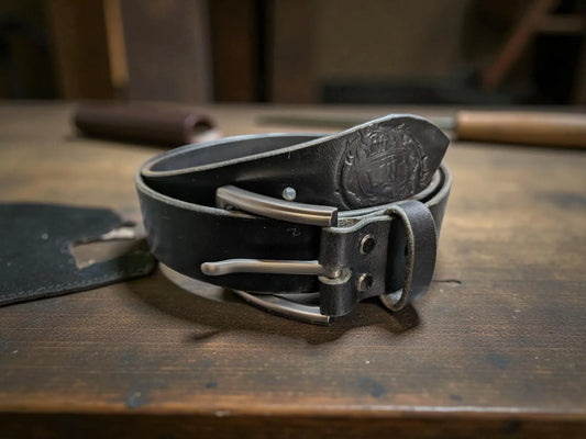 Black leather belt with silver buckle on a wooden surface