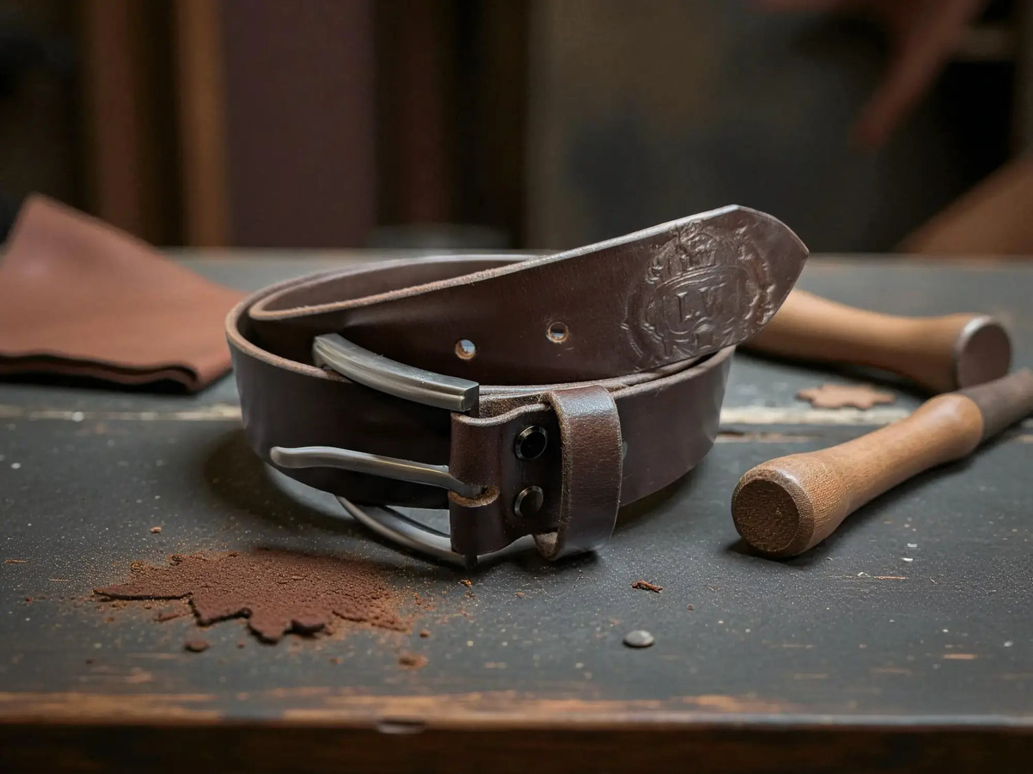 Brown leather belt on a rustic wooden surface with tools in the background