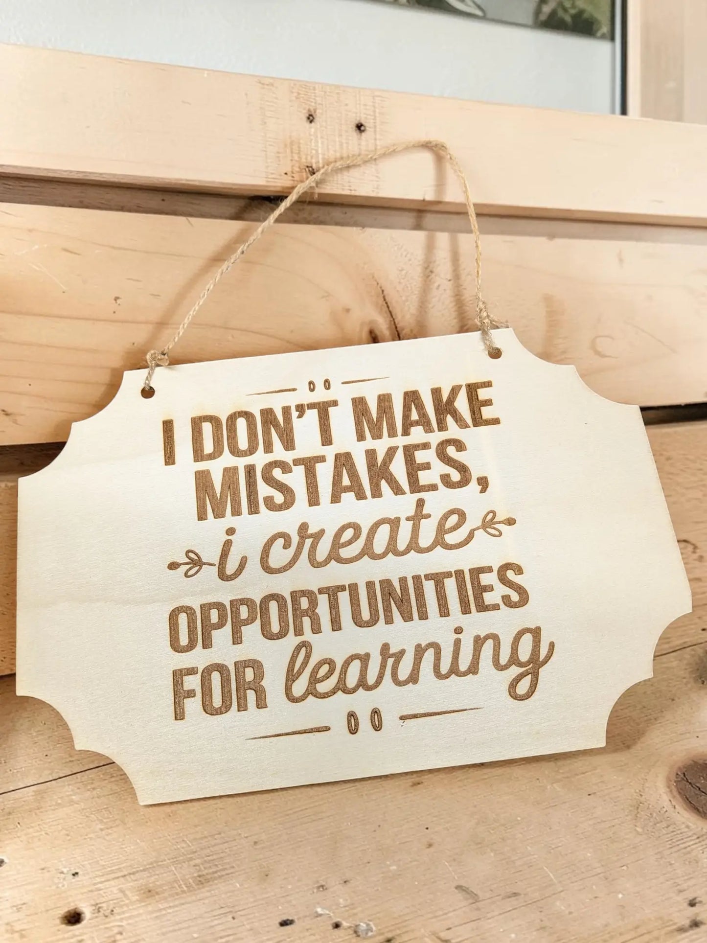 A light-colored basswood hanging wall sign with laser engraved brown motivational quote i dont make mistakes
