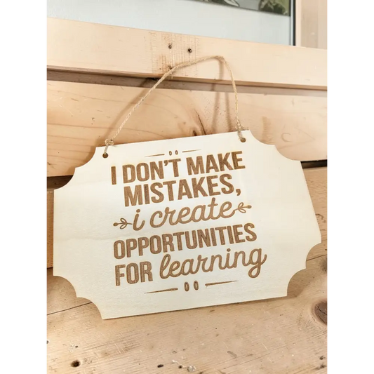 A light-colored basswood hanging wall sign with laser engraved brown motivational quote i dont make mistakes