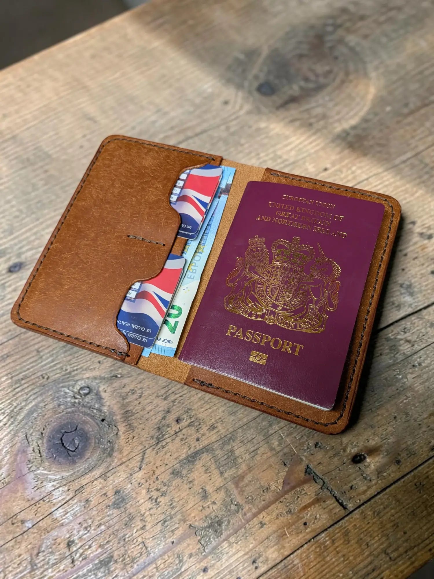 Brown leather passport cover with visible stitching holding a maroon uk passport and banknotes in badalassi pueblo