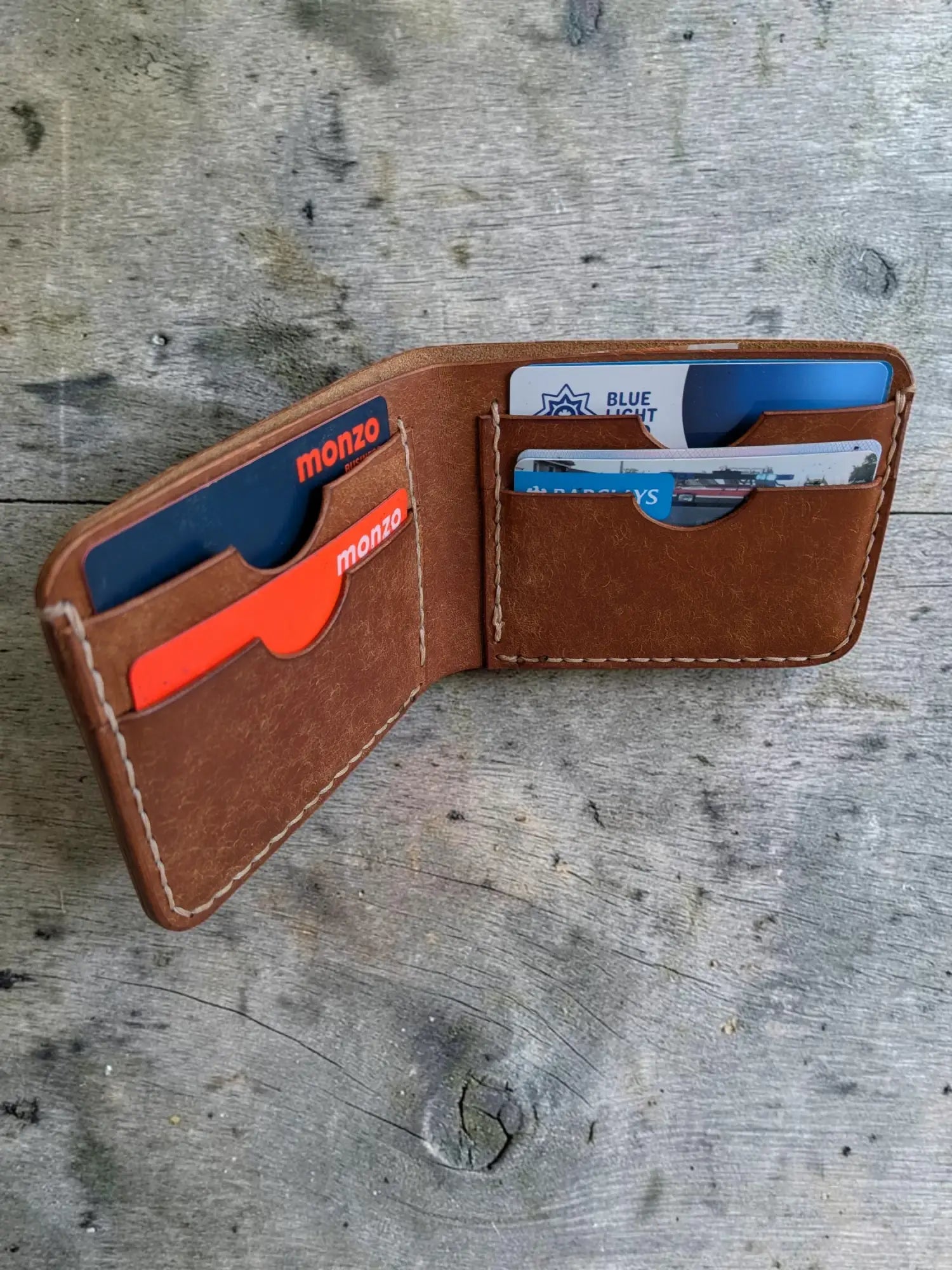 Brown leather bifold wallet with visible stitching and multiple card slots holding credit cards mealstrom badalassi pueblo
