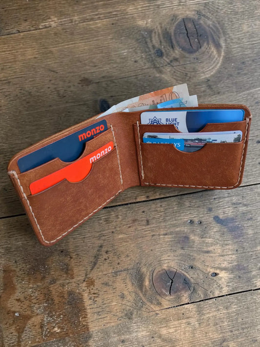 Three tan leather Mealstrom bifold wallets fanned out on a wooden workbench
