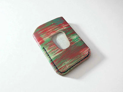 Red and green splash-dyed vegetable tanned leather card wallet showing thumb cutout slot, front view