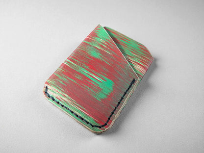 Red and green splash-dyed vegetable tanned leather card wallet, closed, front view on a grey surface