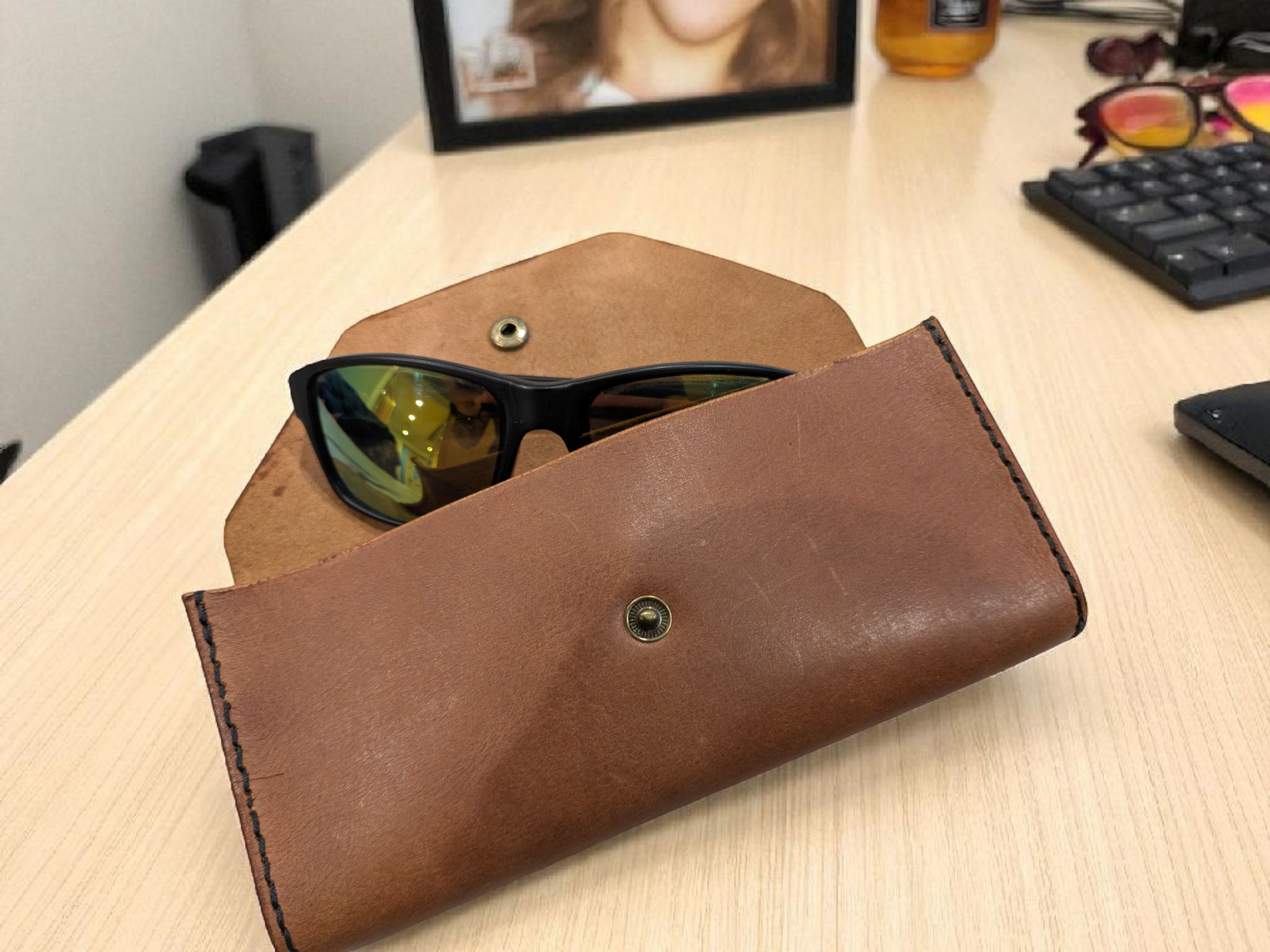 Brown leather sunglasses case with sunglasses inside on a wooden surface.