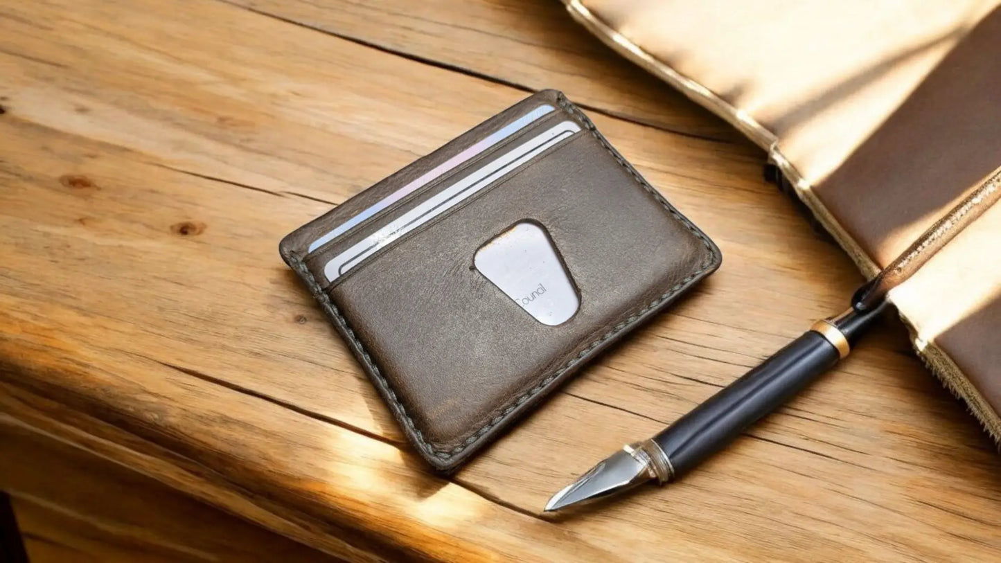 Brown leather Solaris minimalist card holder with an AirTag slot, beside a fountain pen and notebook