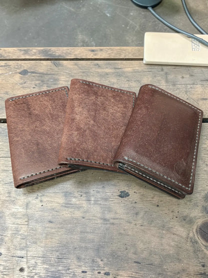 Three brown leather Venturi wallets fanned out on a wooden table showing colour variation